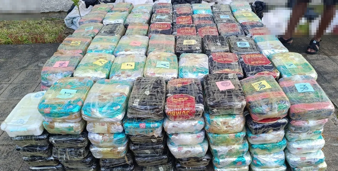 Bricks of methamphetamine from the Beira seizure laid out in rows, February 2025; persons at the edge pixelated